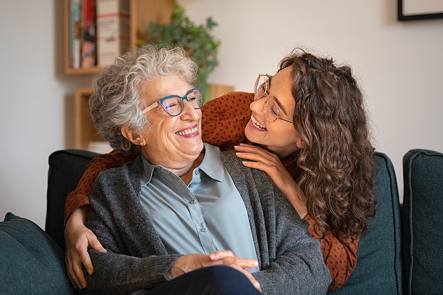 Old grandmother and adult granddaughter hugging at home and look